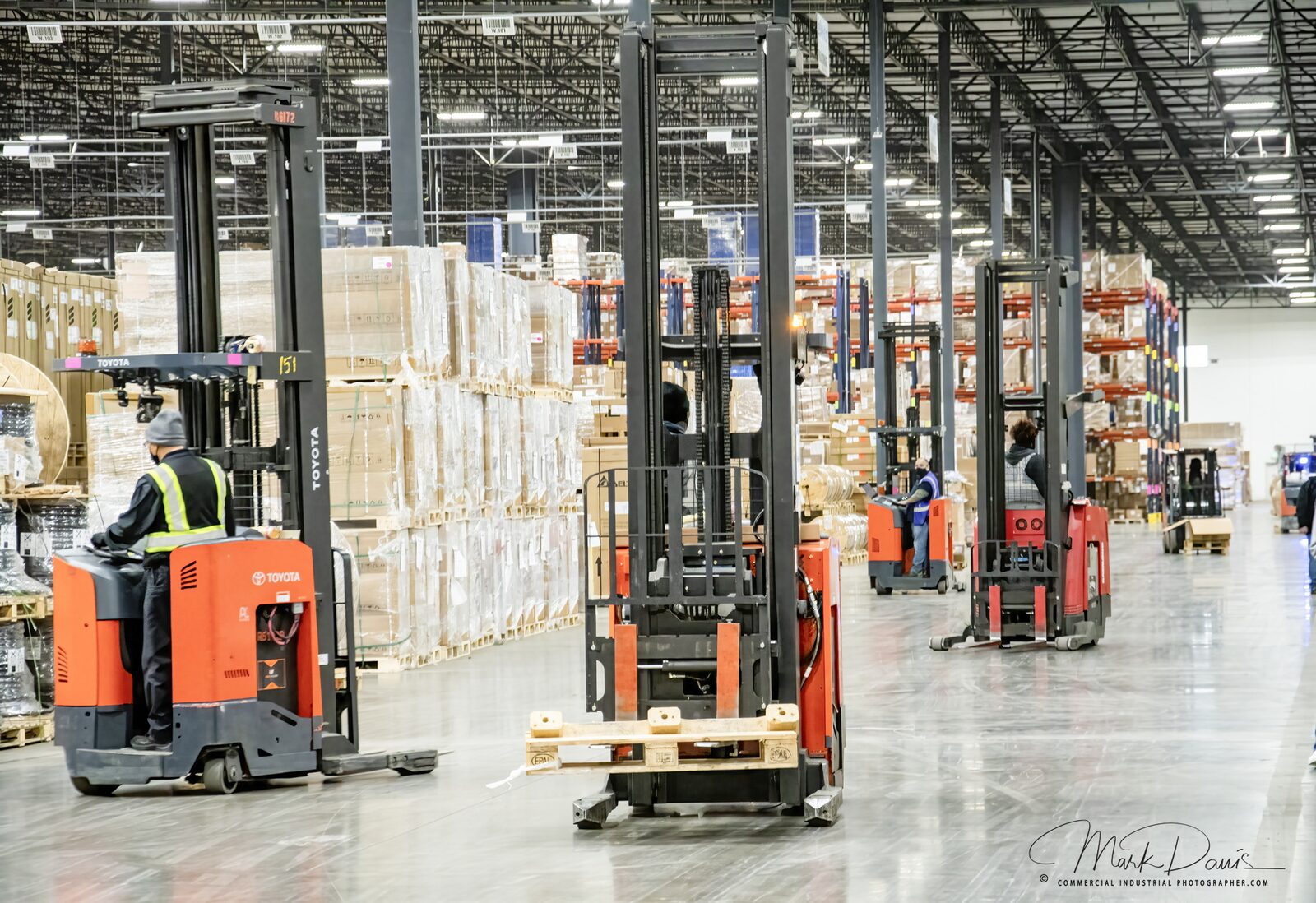 Forklifts operating in a distribution warehouse aisle stacked with pallets